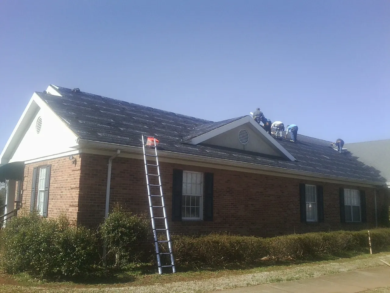 Crew tearing shingles off a brick ranch roof with a ladder set — Metal Roof Repair work by our crew in Williamsville