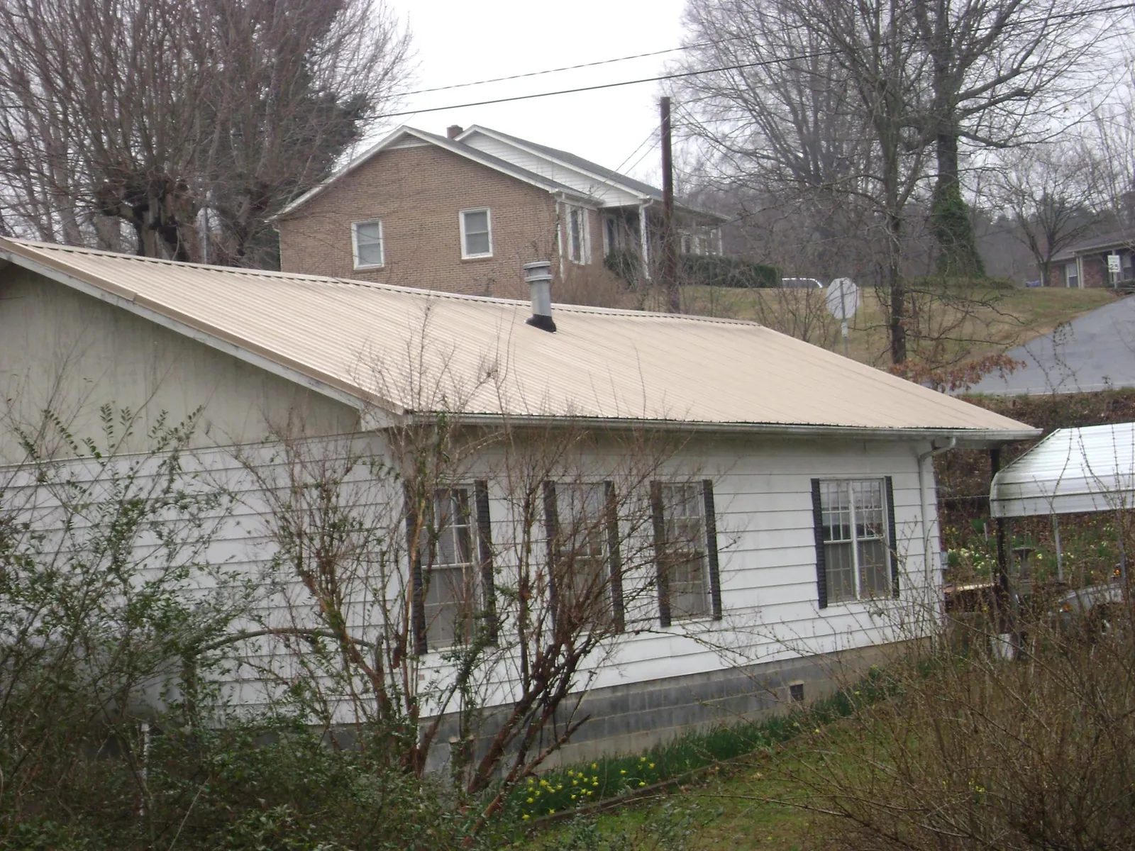 Tan metal roof on a white sided house set into a hillside — Commercial Roofing by Roofing Brothers in Williamsville
